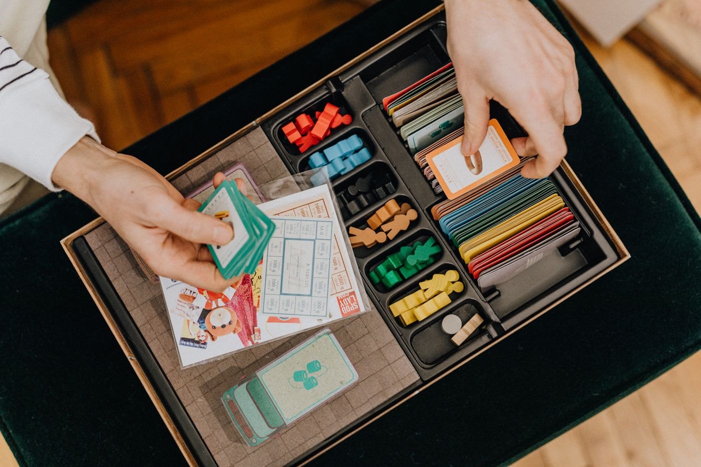 Hands sorting cards and coloured wooden pieces in a board game box