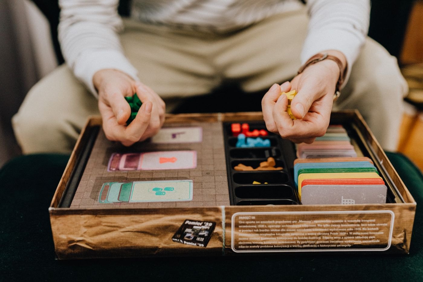 Hands holding coloured wooden game pieces above a compartmented box