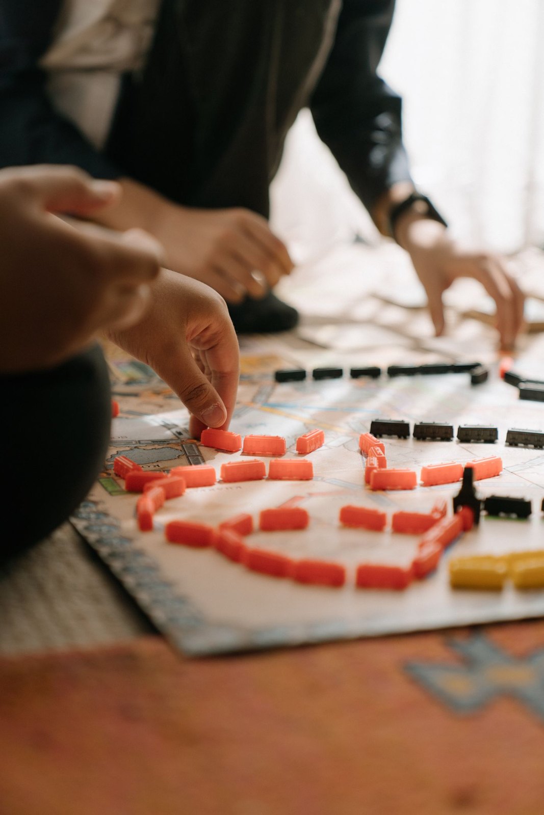 Several hands sharing a map board with coloured train pieces