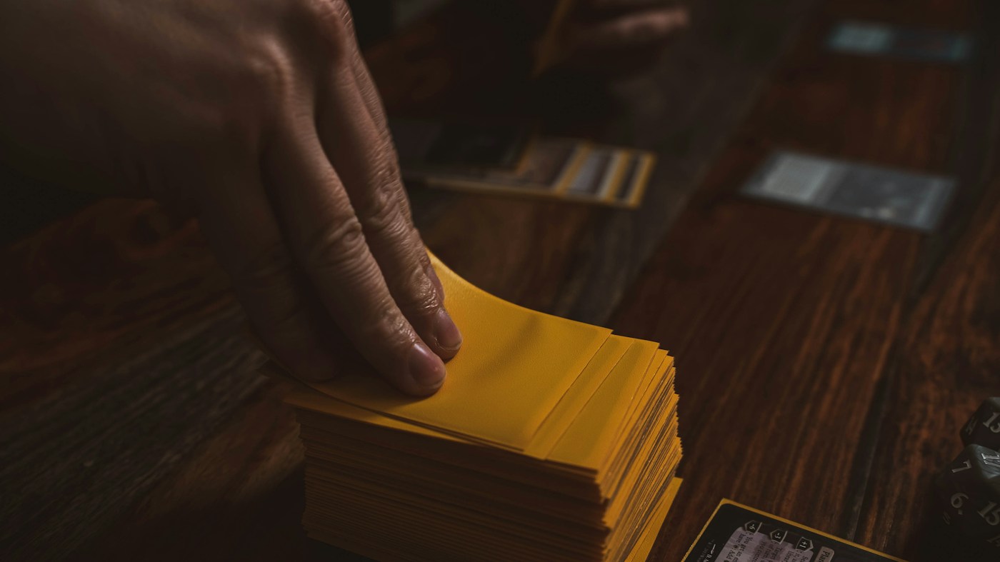 A hand drawing a card from a deck in yellow protective sleeves